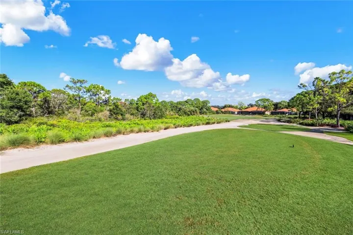 Expansive green space with manicured turf, bordering a paved pathway and lush natural landscaping