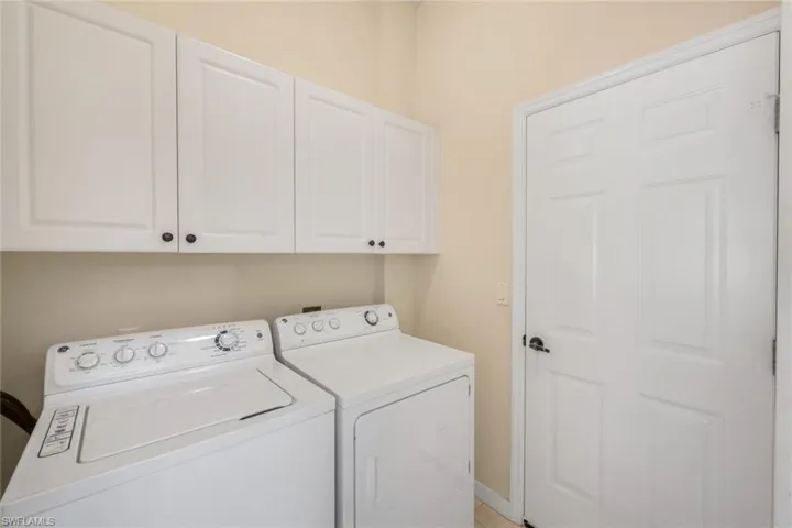 Integrated laundry area featuring white upper cabinetry with dark hardware and a paneled door