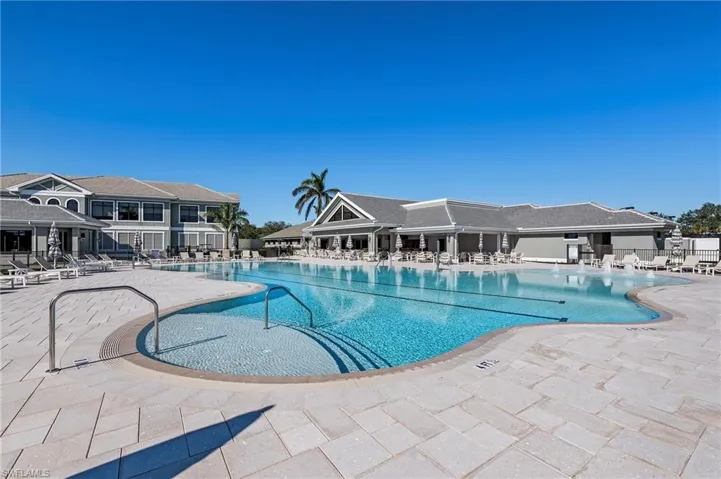 Expansive outdoor swimming pool with integrated steps, surrounding paved patio, and adjacent clubhouse structures