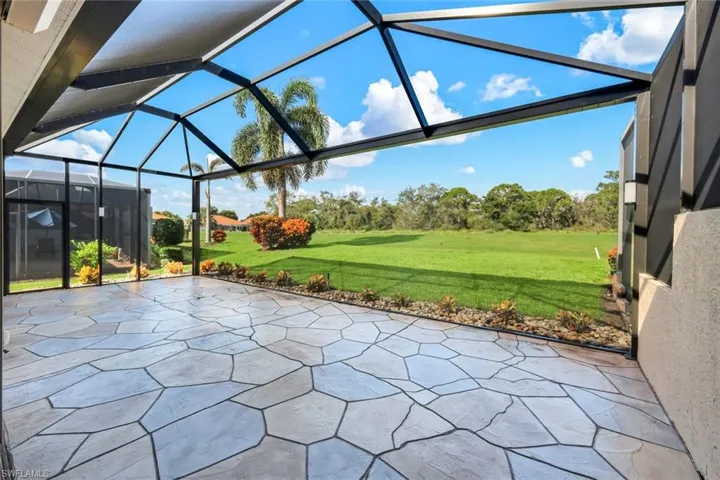 Expansive screened-in patio featuring a geometric paver floor, overlooking a manicured lawn and mature landscaping