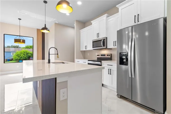 Kitchen featuring appliances with stainless steel finishes, light stone counters, decorative light fixtures, a center island with sink, and white cabinets