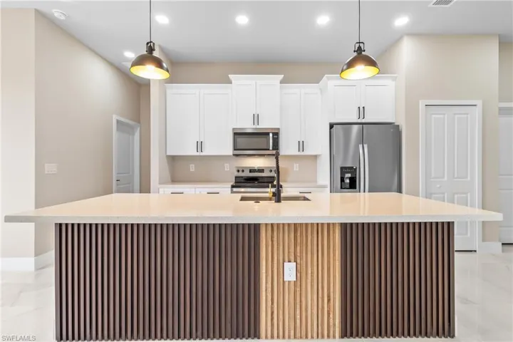 Kitchen featuring stainless steel appliances, light stone counters, a spacious island, recessed lighting, and white cabinetry
