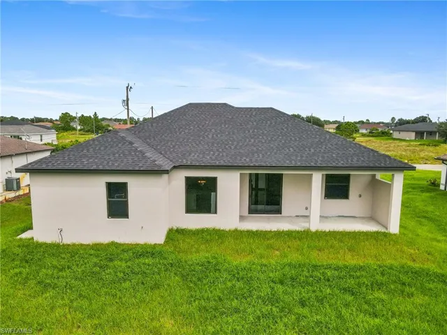 Rear view of property featuring stucco siding, a yard, a patio area, and roof with shingles