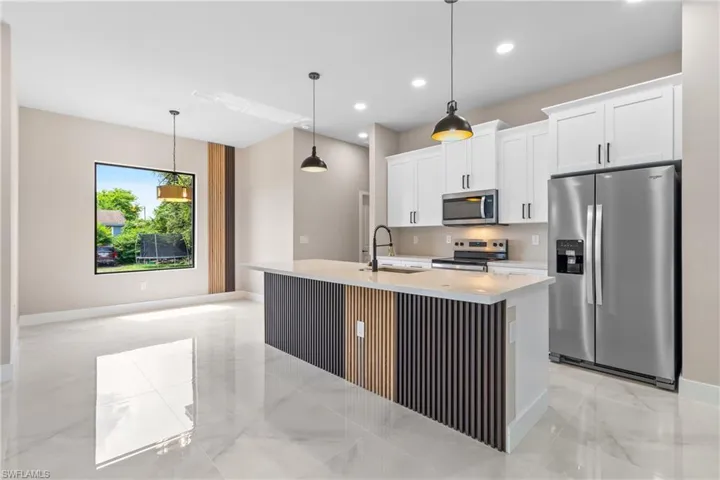 Kitchen featuring appliances with stainless steel finishes, decorative light fixtures, a center island with sink, light marble finish floors, and recessed lighting