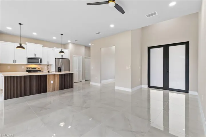Kitchen with white cabinets, appliances with stainless steel finishes, open floor plan, hanging light fixtures, and a kitchen island with sink
