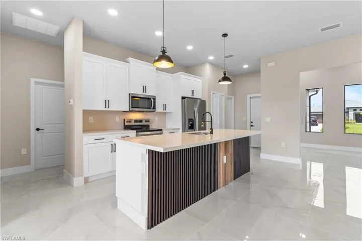 Kitchen featuring an island with sink, pendant lighting, white cabinets, appliances with stainless steel finishes, and recessed lighting