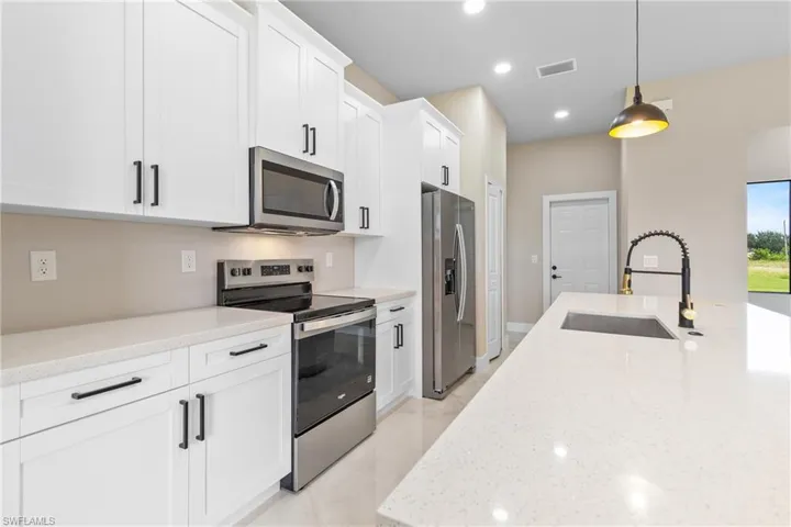Kitchen with appliances with stainless steel finishes, light stone countertops, white cabinets, recessed lighting, and hanging light fixtures