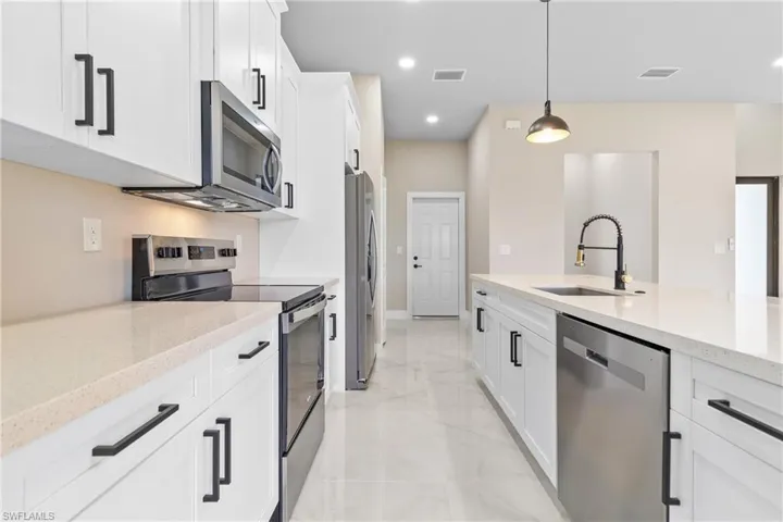 Kitchen with stainless steel appliances, light stone countertops, white cabinetry, recessed lighting, and decorative light fixtures