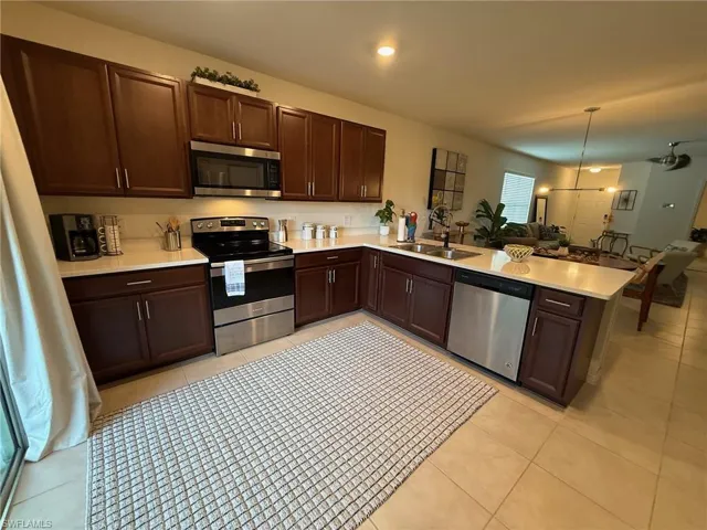 Kitchen featuring appliances with stainless steel finishes, dark brown cabinetry, a peninsula, open floor plan, and hanging light fixtures