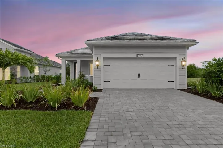 Coastal-elevation curb appeal with a Slate paver driveway, extended two-car garage, and black coach lighting beneath a concrete tile roof, built with whole-house hurricane impact glass in the gated Verandah golf community.