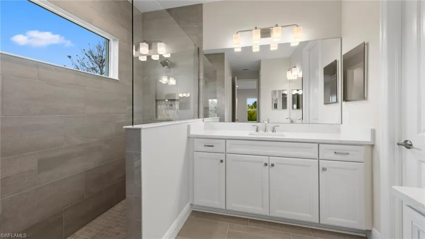 A walk-in shower clad in large-format grey tile and a dual-sink quartz vanity are brightened by a clerestory window.