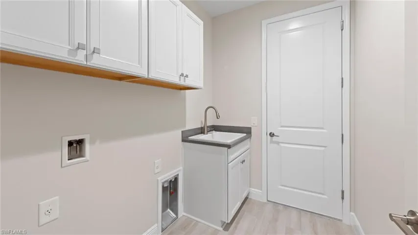 A spacious laundry room with white Wentworth cabinetry, a Corian-topped utility sink, and wood-look tile flooring adds everyday function.
