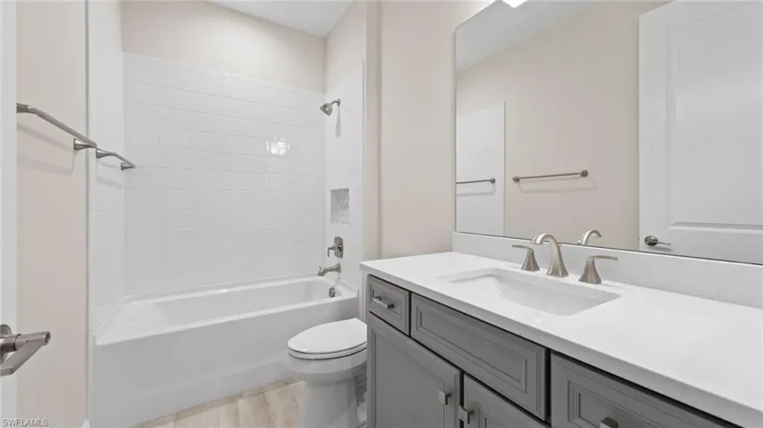 The guest bath pairs a Stone Gray vanity with Ethereal White quartz, a white-tiled tub-shower combination, and brushed-nickel fixtures.