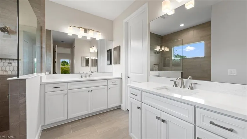 A spa-inspired owner's bath with a dual-sink vanity in Ashen Grey quartz, white Wentworth cabinetry, large-format grey tile, and a glass walk-in shower finished with brushed-nickel trim.
