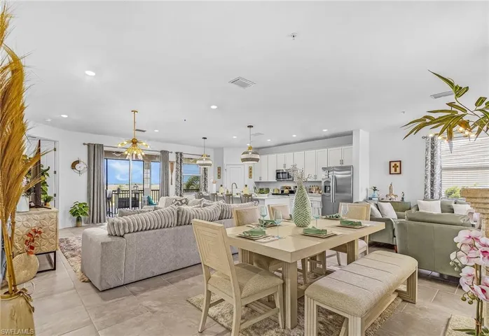 Open-concept living space featuring large format tile flooring, a dining area with a rectangular table and bench seating, and a kitchen with white cabinetry and stainless steel appliances