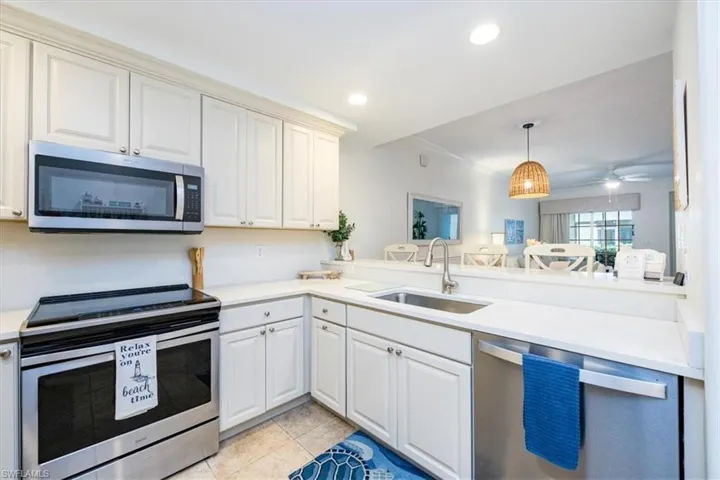 Kitchen with stainless steel appliances, quartz countertops, light tile floors, sink, white cabinets, and breakfast bar