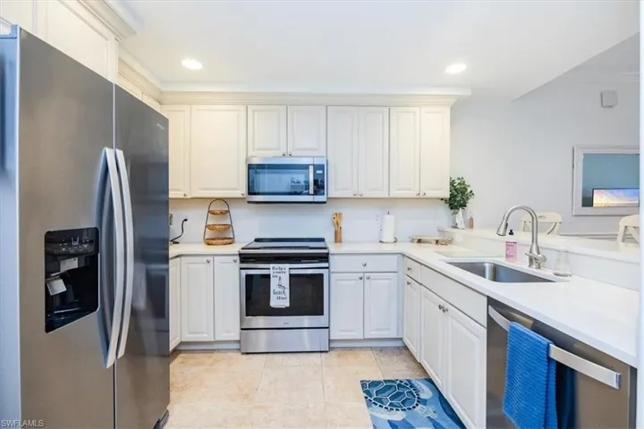 Kitchen with stainless steel appliances, quartz countertops, light tile floors, sink, white cabinets, and breakfast bar