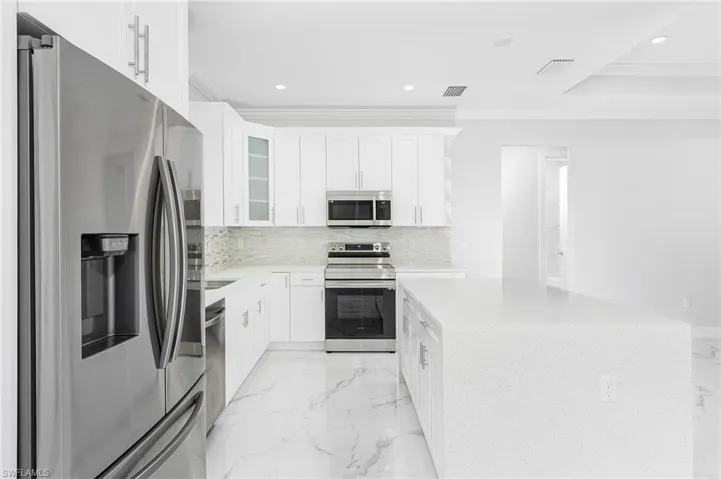 Kitchen featuring stainless steel appliances, backsplash, light tile floors, ornamental molding, and white cabinetry
