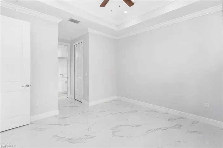 Spare room featuring a raised ceiling, ceiling fan, light tile floors, and crown molding