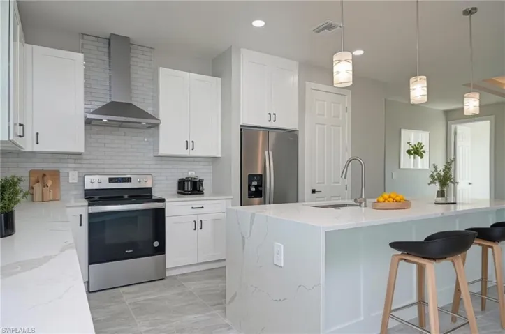 Kitchen featuring stainless steel appliances, pendant lighting, light stone countertops, a kitchen bar, and white cabinetry