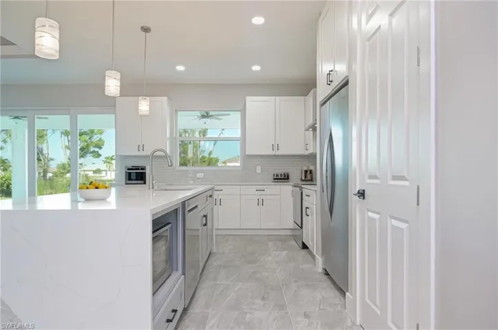 Kitchen with white cabinetry, decorative light fixtures, light stone counters, and stainless steel appliances