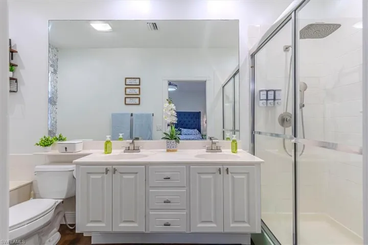 Bathroom featuring double vanity, connected bathroom, a shower stall, and dark wood-style flooring