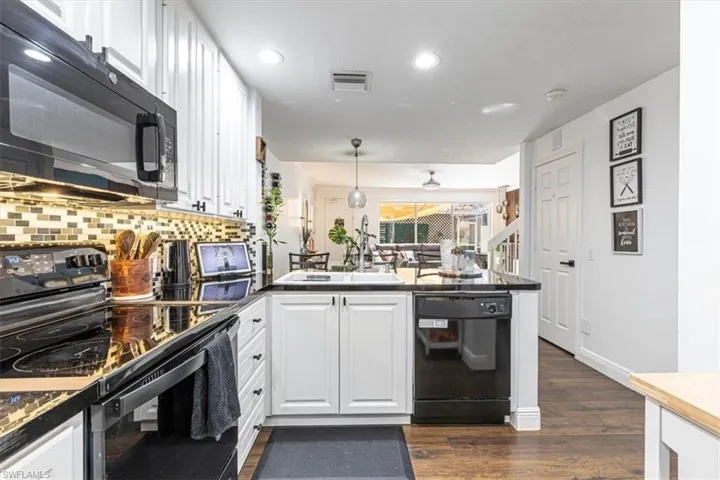 Kitchen featuring black appliances, a peninsula, white cabinetry, dark wood-type flooring, and decorative light fixtures