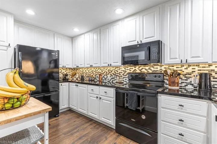 Kitchen with black appliances, white cabinetry, dark wood finished floors, dark stone countertops, and recessed lighting