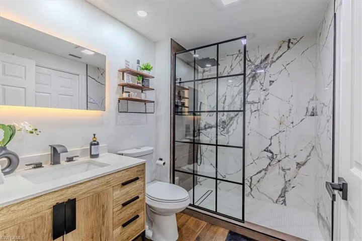 Full bath with a marble finish shower, vanity, dark wood-style flooring, and recessed lighting
