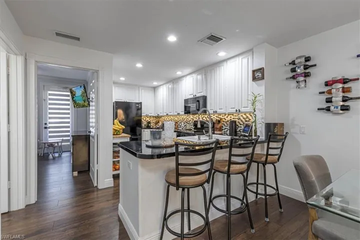 Kitchen with a peninsula, white cabinets, black appliances, dark wood-style flooring, and tasteful backsplash