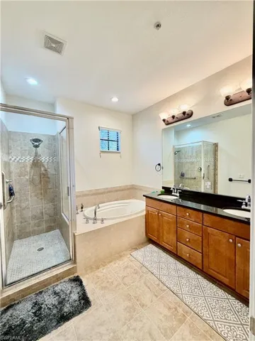 Full bathroom featuring double vanity, a stall shower, a garden tub, and light tile patterned floors