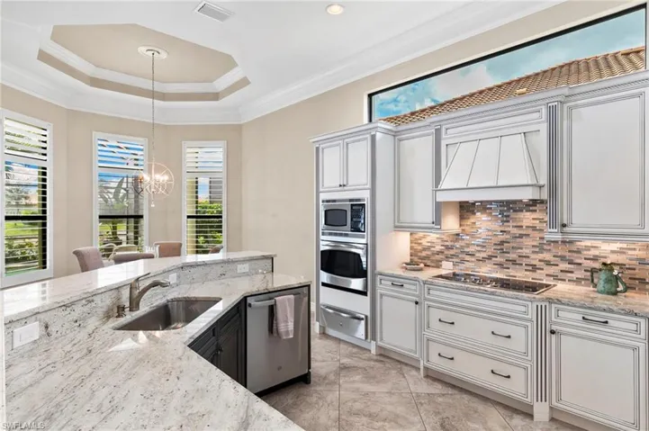 Two tone kitchen with crown molding, light stone counters, a chandelier, stainless steel appliances, and a warming drawer