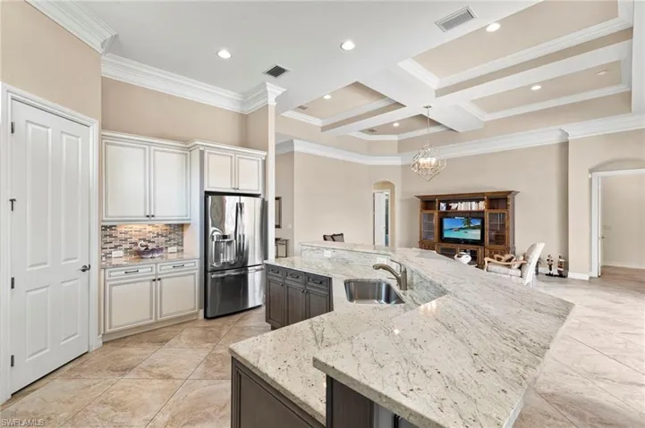 Kitchen with two tone cabinets, arched walkways, stainless steel fridge, coffered ceiling, and light stone countertops
