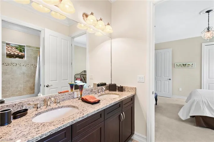 Ensuite bathroom featuring double vanity, light carpet, ornamental molding, hanging lights, and shower / bath combo with shower curtain