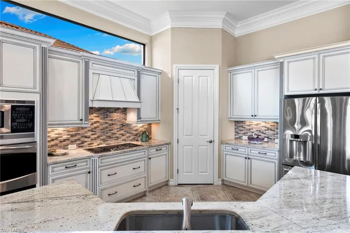 Kitchen featuring stainless steel appliances, light stone countertops, ornamental molding, and tasteful backsplash