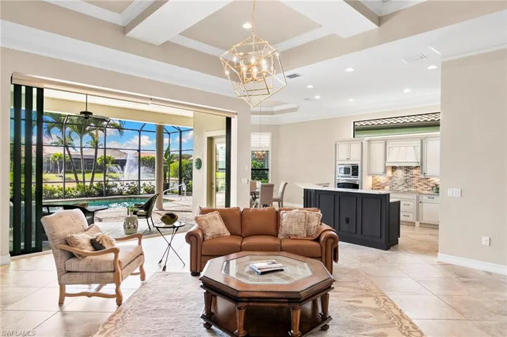 Living room featuring ornamental molding, a ceiling fan, coffered ceiling, a chandelier, and light tile patterned flooring