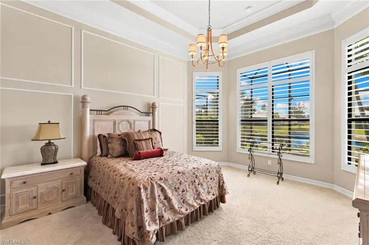 Bedroom featuring a chandelier, light colored carpet, a tray ceiling, crown molding, and a decorative wall