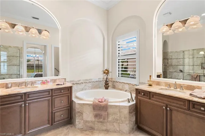 Full bathroom with a shower stall, a garden tub, two vanities, and ornamental molding