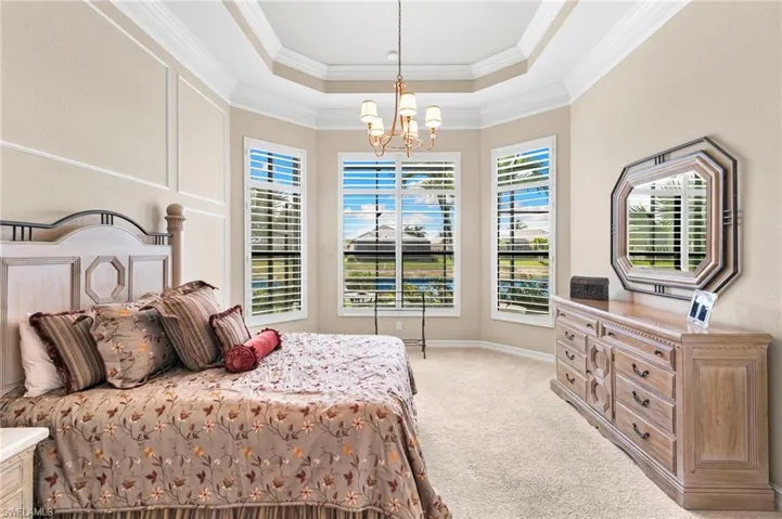 Bedroom featuring hanging lights, light carpet, a tray ceiling, and crown molding