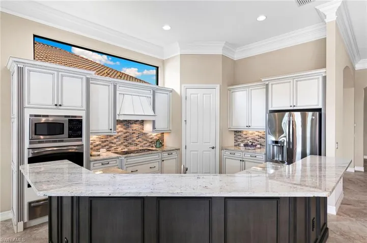 Two tone kitchen featuring backsplash, stainless steel appliances, light stone countertops, a spacious island, and ornamental molding