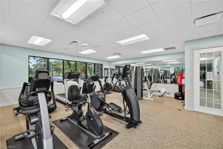 Dedicated fitness room featuring multiple exercise machines, mirrored wall, and large windows