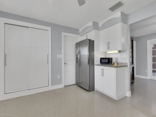 Kitchen featuring stainless steel refrigerator with ice dispenser, light stone counters, white cabinetry, and a textured ceiling
