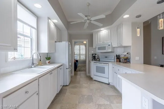 Kitchen with ornamental molding, white appliances, ceiling fan, decorative light fixtures, and white cabinetry