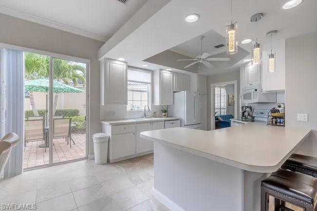 Kitchen with kitchen peninsula, a kitchen breakfast bar, white appliances, and white cabinetry