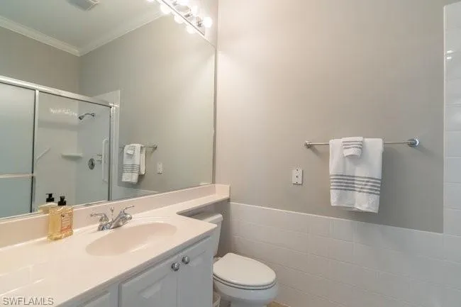 Bathroom featuring walk in shower, crown molding, toilet, vanity, and tile walls