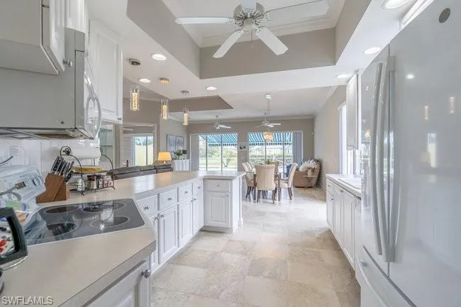 Kitchen featuring pendant lighting, white appliances, a tray ceiling, decorative backsplash, and white cabinets