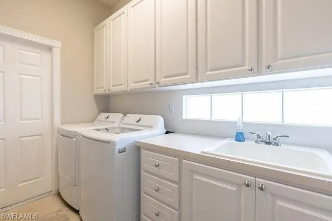 Laundry area featuring washing machine and clothes dryer, sink, and cabinets