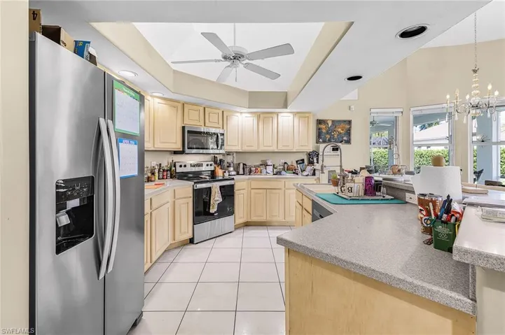 Kitchen with stainless steel appliances, a tray ceiling, a ceiling fan, light tile patterned floors, and light wood finish cabinetry