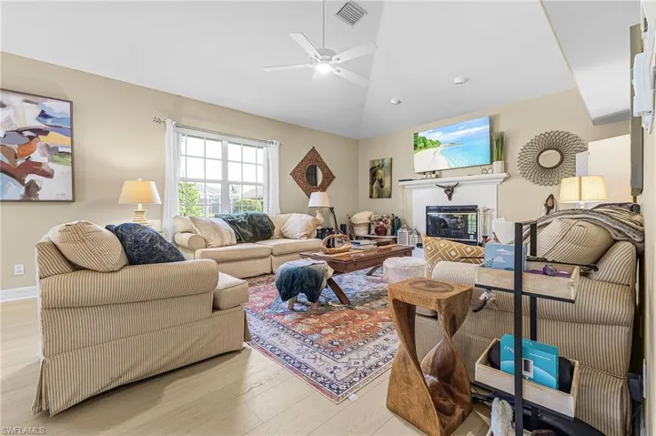 Living room with wood finished floors, vaulted ceiling, a glass covered fireplace, and a ceiling fan