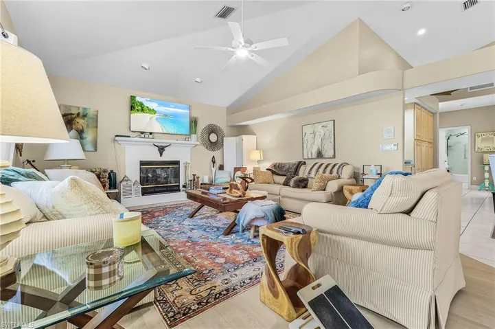 Living area with a ceiling fan, a glass covered fireplace, light wood-type flooring, and lofted ceiling